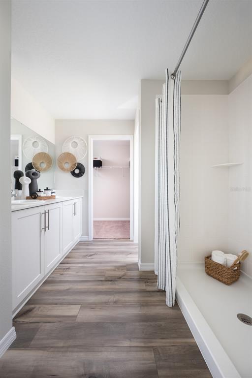 A bathroom features white cabinets, wood-look flooring, a walk-in shower, and a doorway to a closet — 1707 VANILLA STREET, HAINES CITY, FL