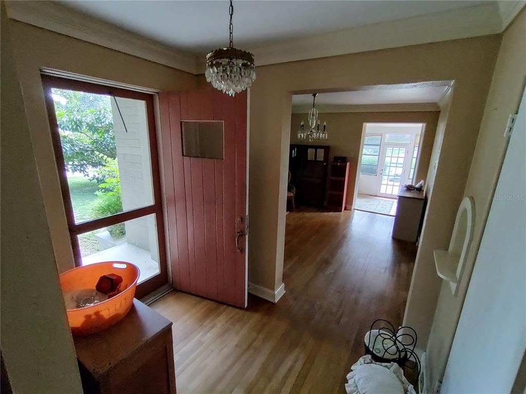 An entryway with hardwood floors, a crystal chandelier, and a red front door — 995 W 11TH AVENUE, MOUNT DORA, FL
