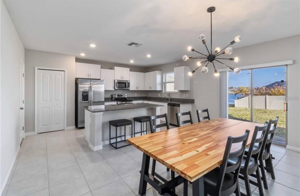 A kitchen with white cabinets, granite countertops, and a dining area with a wooden table — 5478 GRAYS HARBOR COURT, WIMAUMA, FL