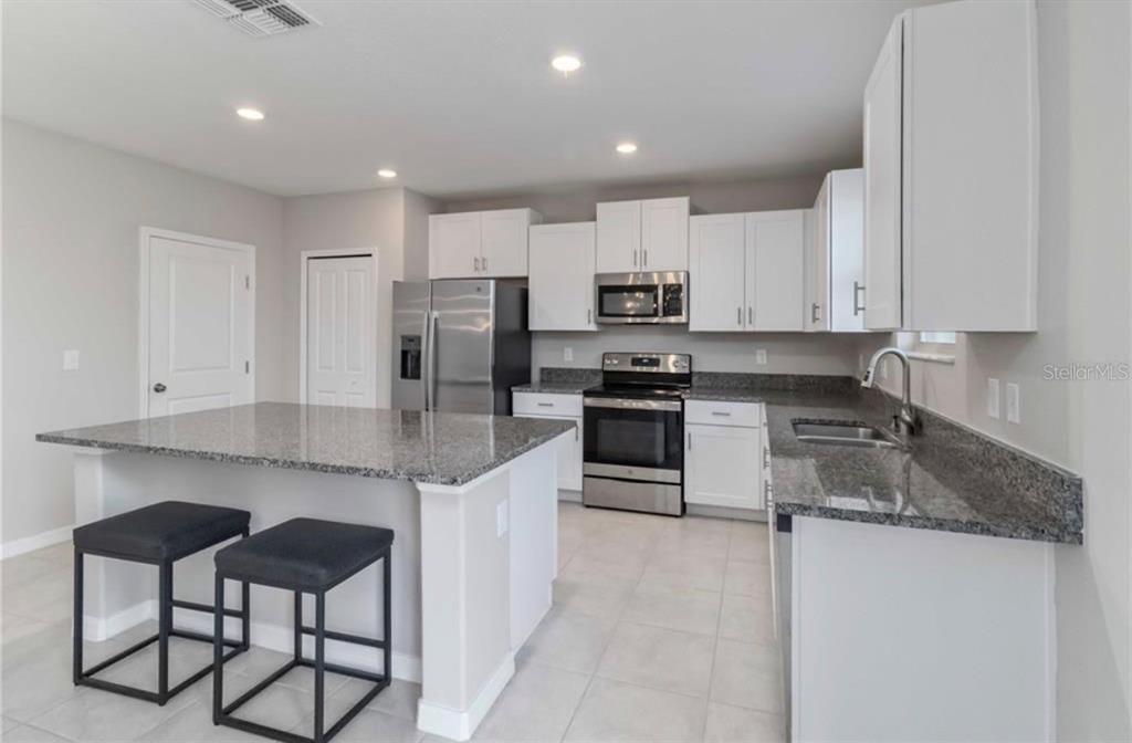 A modern kitchen features white cabinets, granite countertops, stainless steel appliances, and a breakfast island — 5478 GRAYS HARBOR COURT, WIMAUMA, FL
