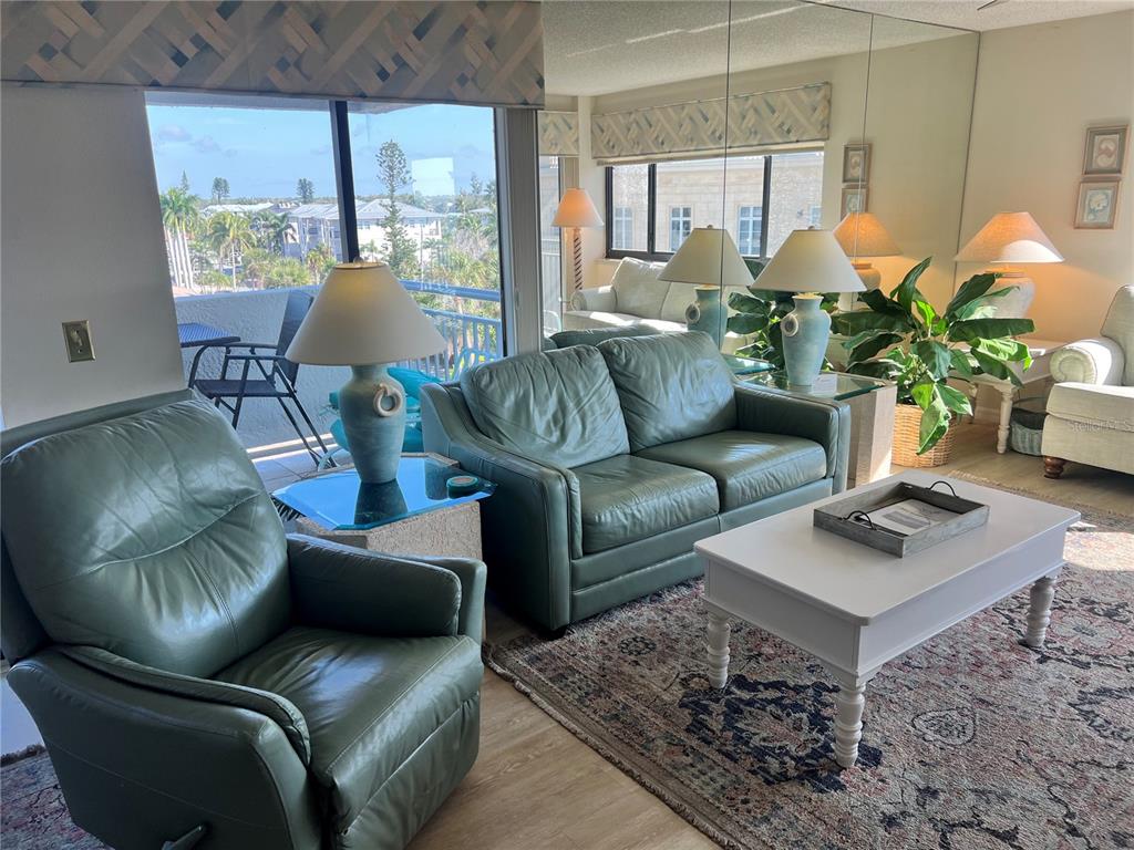 A living room features green leather furniture, a white coffee table, and a mirrored wall — 1001 POINT OF ROCKS ROAD UNIT 508, SARASOTA, FL