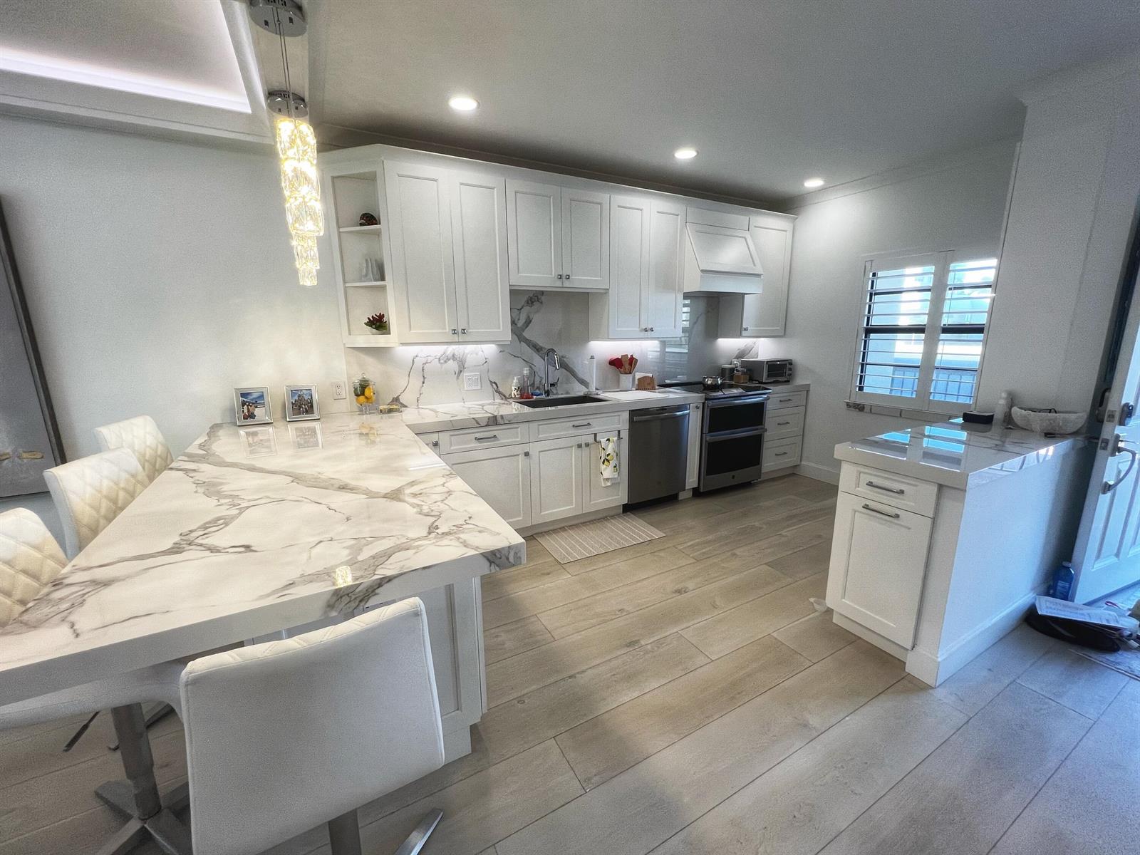 A modern kitchen features white cabinetry, marble-patterned countertops, and light wood-look flooring — 275 S Beach Road # B201, Tequesta FL 33469, TEQUESTA, FL