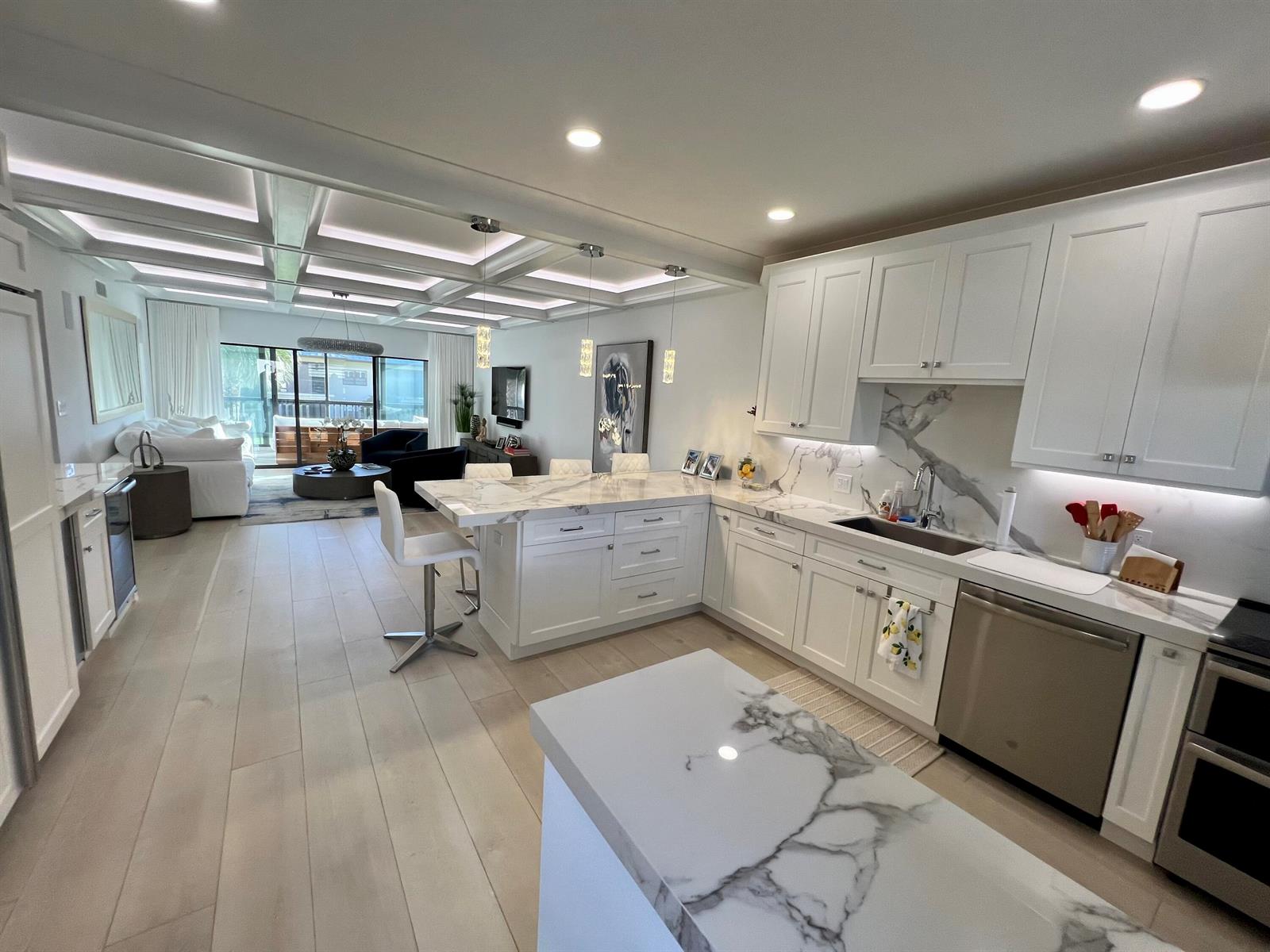 A modern kitchen with white cabinetry and marble countertops opens into a living room area — 275 S Beach Road # B201, Tequesta FL 33469, TEQUESTA, FL