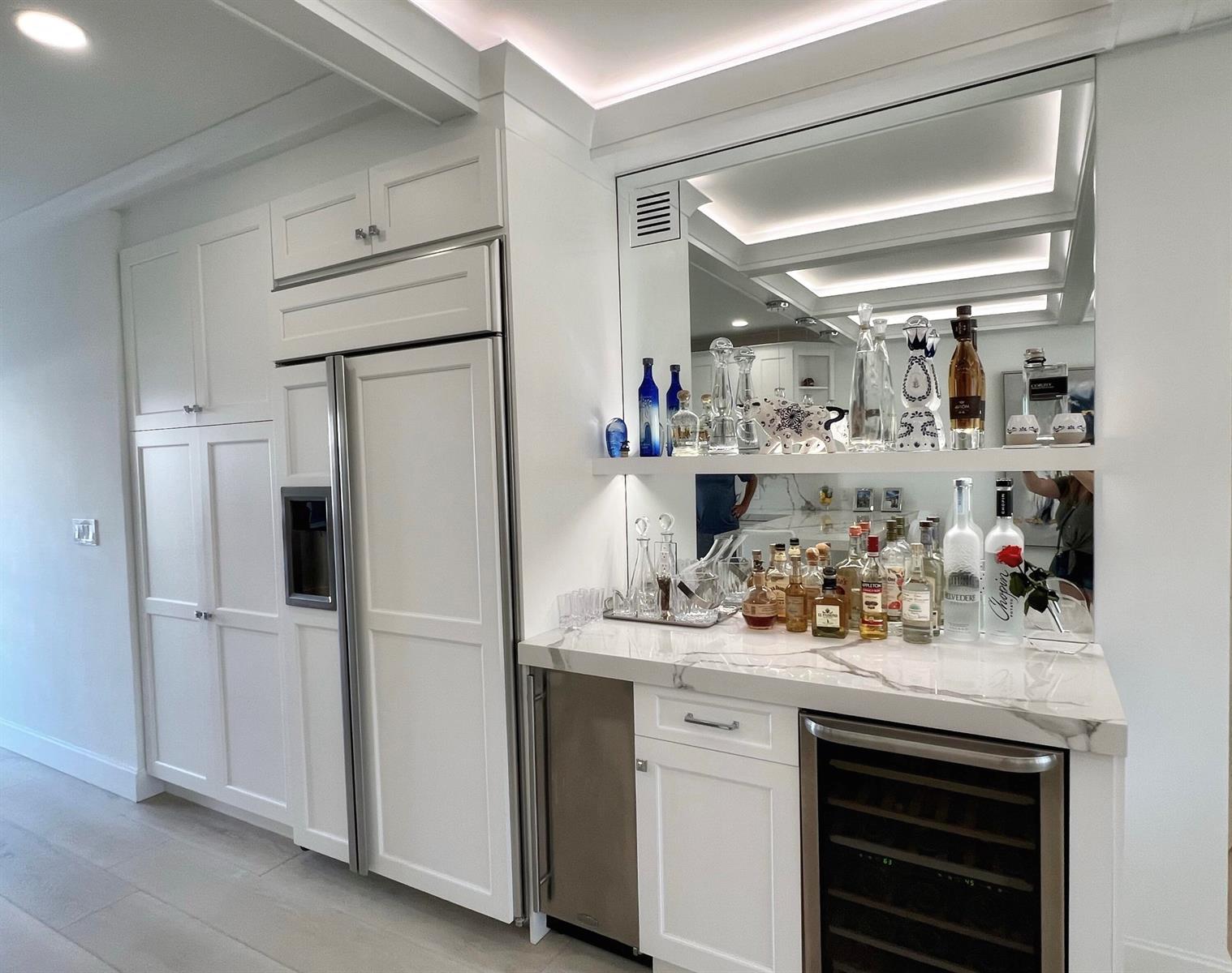 A white kitchen features a built-in refrigerator, marble-topped wet bar, and mirrored shelving — 275 S Beach Road # B201, Tequesta FL 33469, TEQUESTA, FL
