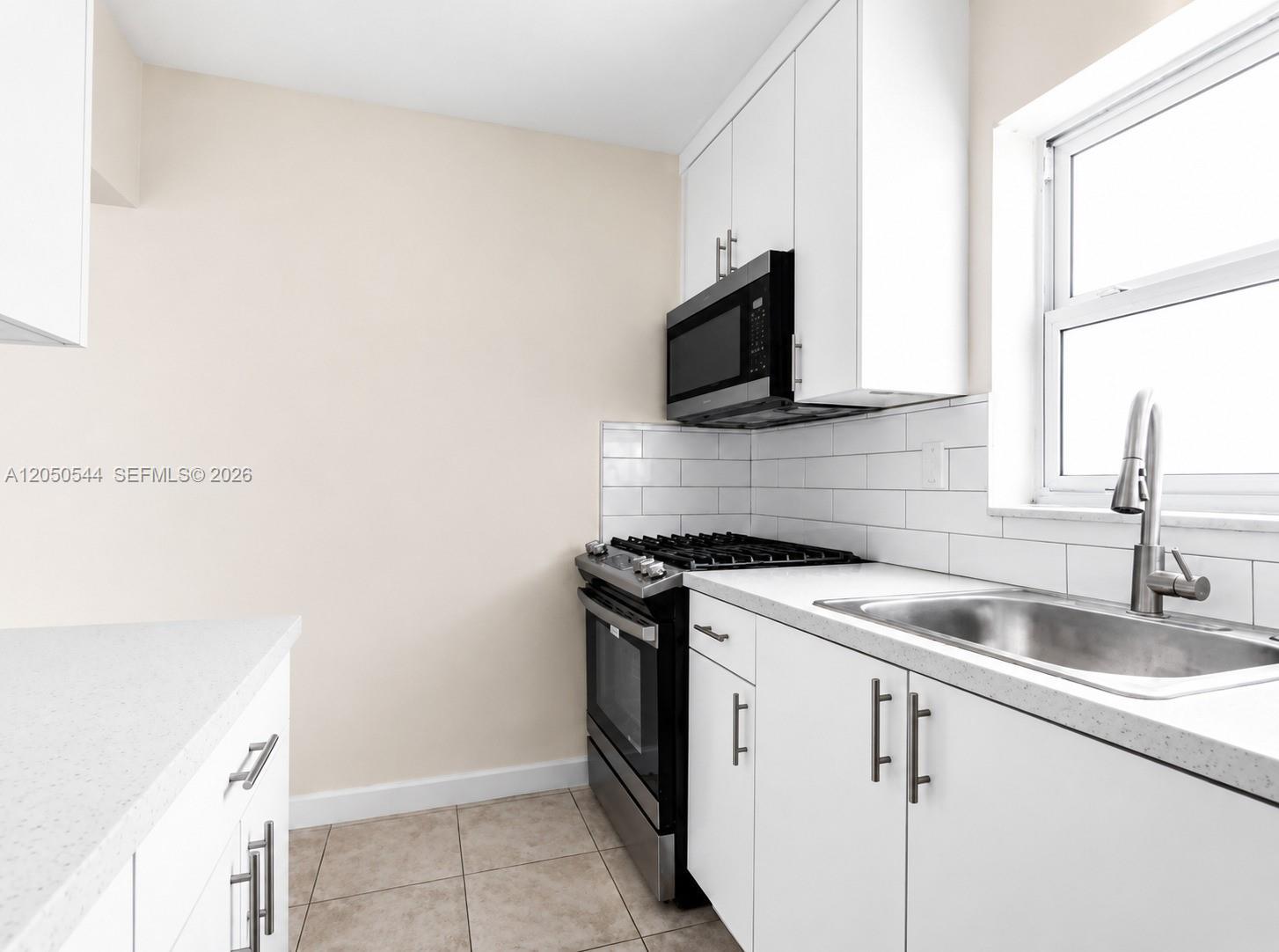 A kitchen features white cabinets, stainless steel appliances, a subway tile backsplash, and tile flooring — 1245 W 24th St # 219, Hialeah FL 33010, HIALEAH, FL