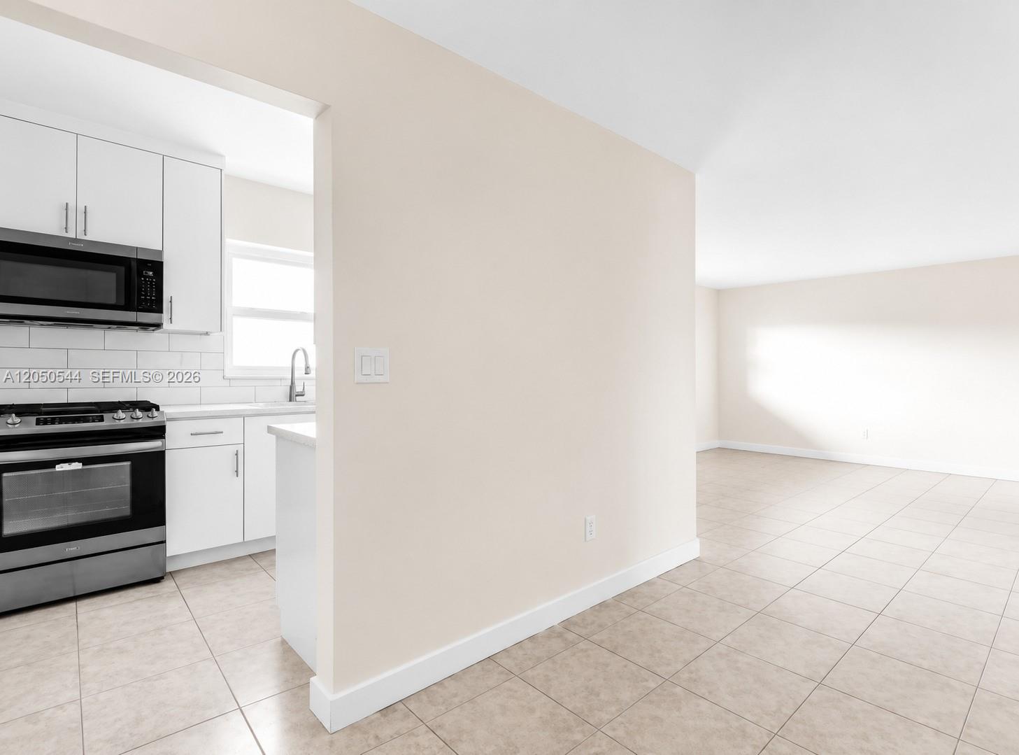A kitchen with white cabinets and stainless steel appliances opens into a tiled living area — 1245 W 24th St # 219, Hialeah FL 33010, HIALEAH, FL