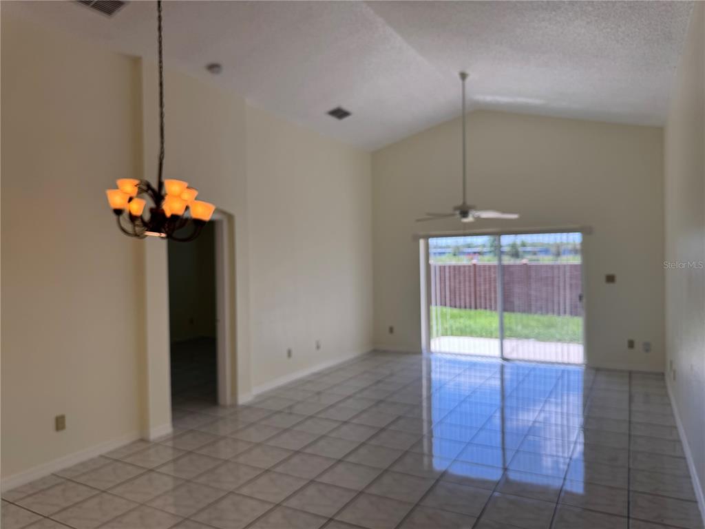 A living room with vaulted ceilings, tile flooring, a chandelier, and a sliding glass door — 7872 ELMSTONE CIRCLE, ORLANDO, FL