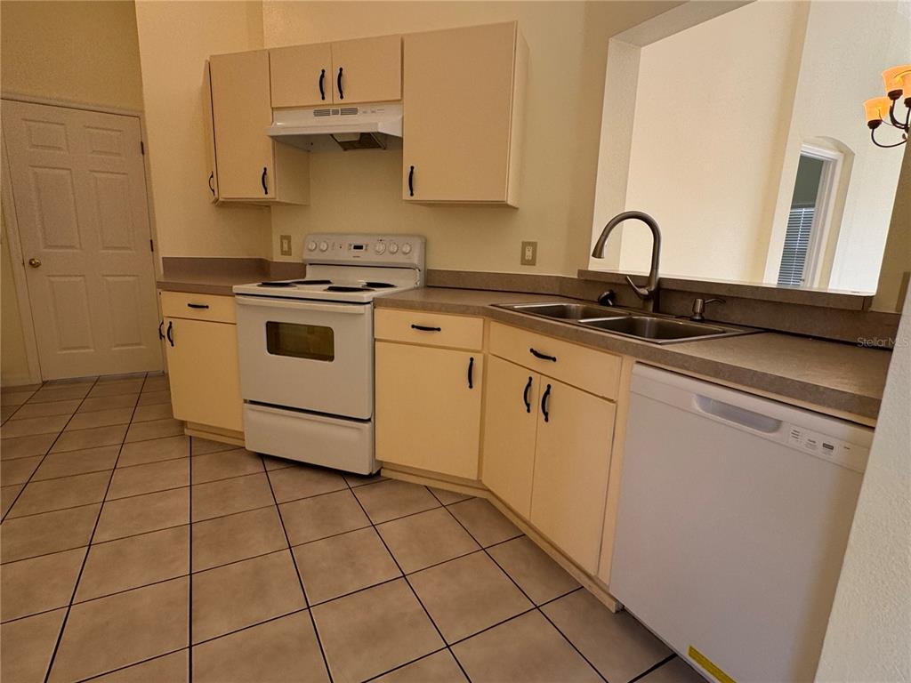 A kitchen features light yellow cabinets, a white stove, a double sink, and tiled flooring — 7872 ELMSTONE CIRCLE, ORLANDO, FL