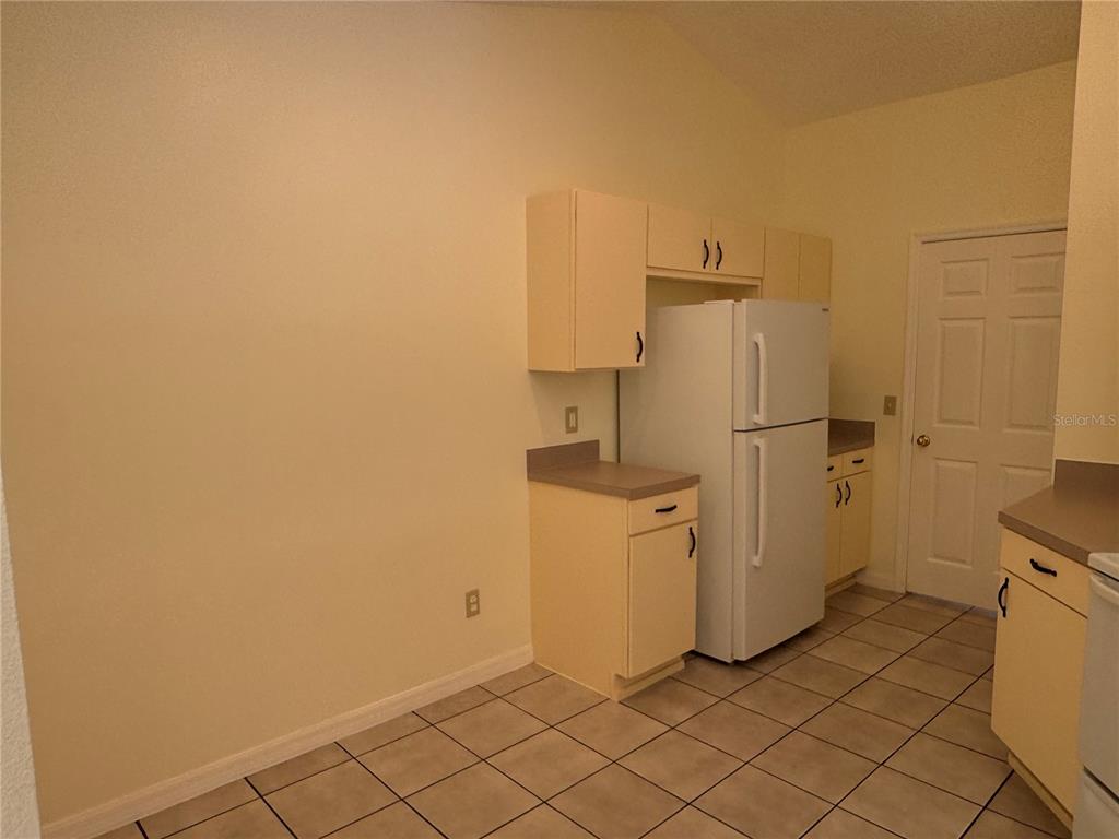 A kitchen features light-colored cabinets, a white refrigerator, and tiled flooring — 7872 ELMSTONE CIRCLE, ORLANDO, FL