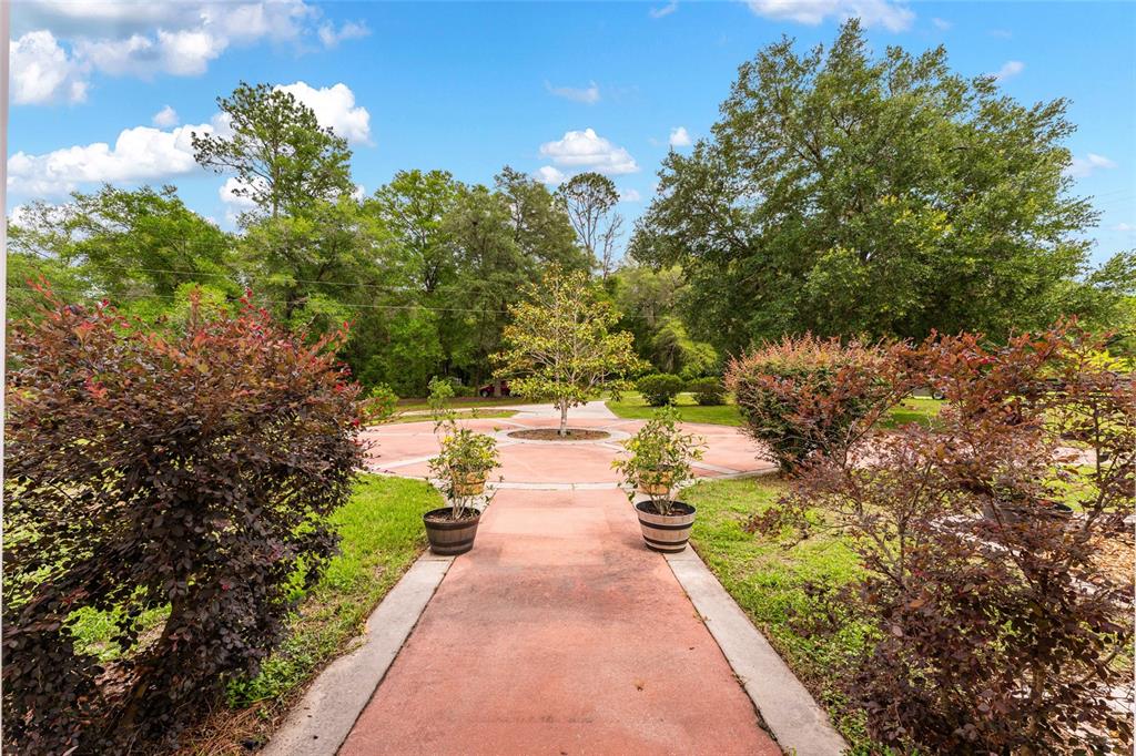 A paved walkway leads to a circular patio featuring a central tree and potted plants — 15510 SW 149TH PLACE, ARCHER, FL