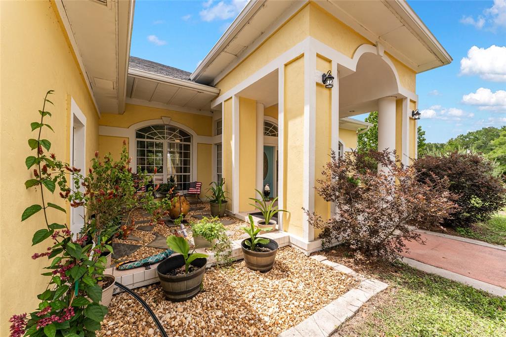 The exterior of a yellow house features a covered entryway with white columns and landscaping — 15510 SW 149TH PLACE, ARCHER, FL