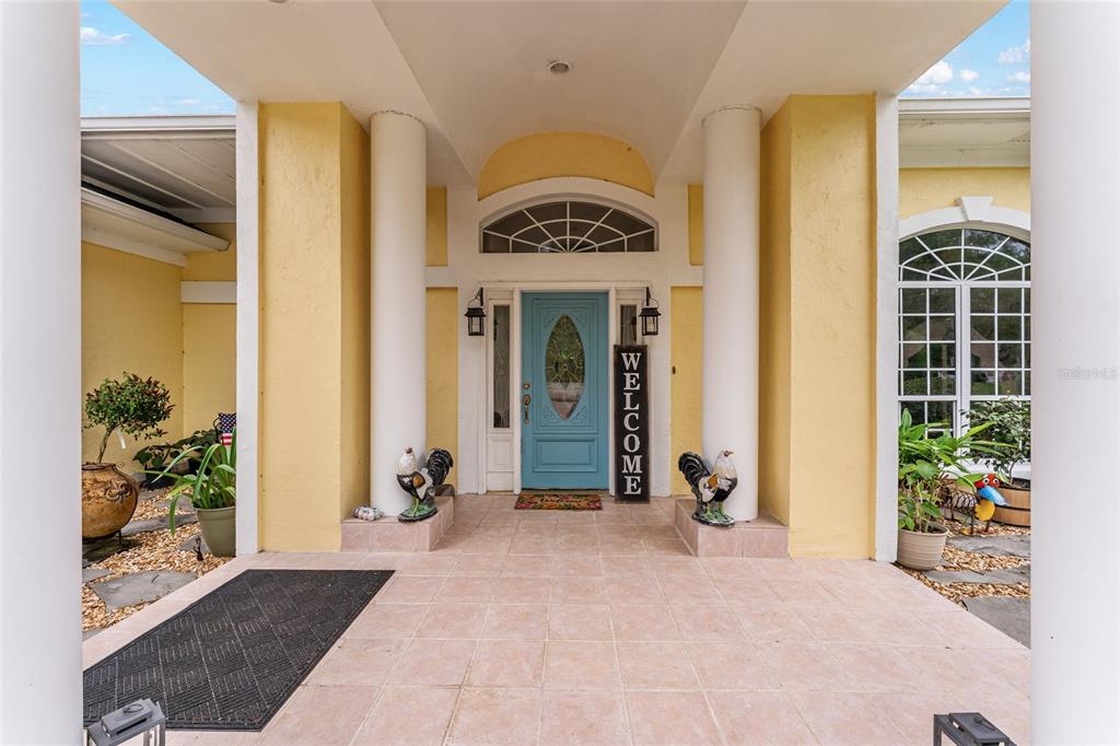 A covered entryway features a light blue front door, yellow walls, and two decorative roosters — 15510 SW 149TH PLACE, ARCHER, FL