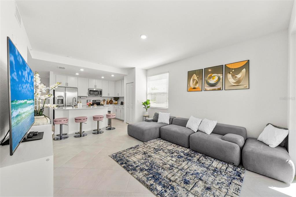 A living room with a grey sectional sofa, a patterned rug, and an open kitchen — 12280 WELLEN GOLF STREET UNIT 101, VENICE, FL