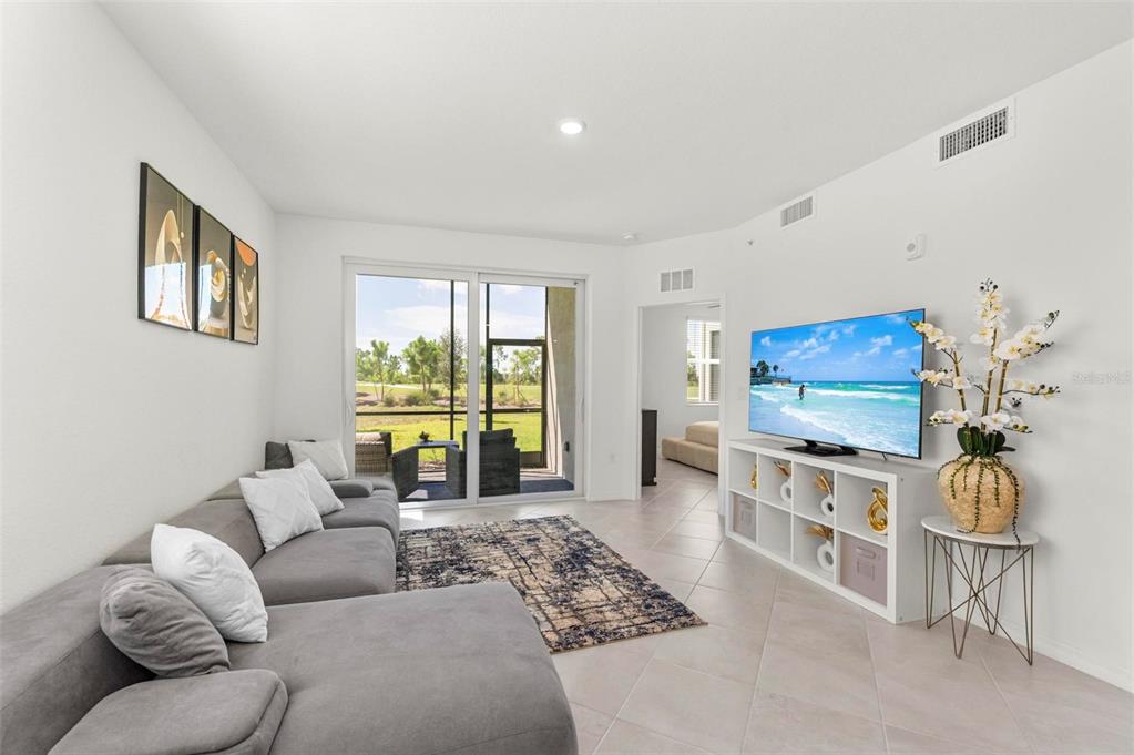 A living room features a gray sectional sofa, a television on a white shelf, and sliding doors — 12280 WELLEN GOLF STREET UNIT 101, VENICE, FL