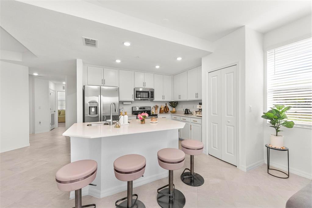 A modern kitchen features white cabinetry, stainless steel appliances, a quartz island, and pink stools — 12280 WELLEN GOLF STREET UNIT 101, VENICE, FL