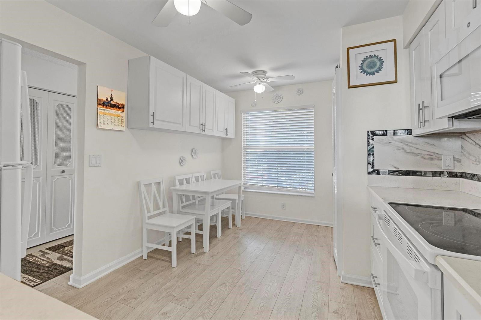 A bright kitchen features white cabinets, a small dining table with chairs, and wood-look flooring — 14575 Bonaire Boulevard # 202, Delray Beach FL 33446, DELRAY BEACH, FL