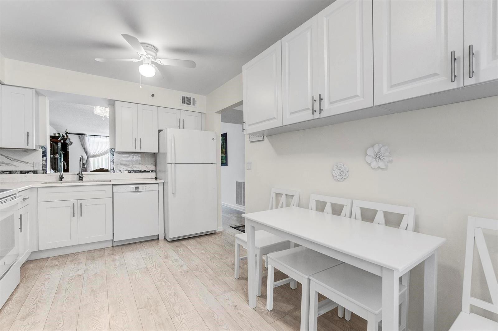 A white kitchen features light wood-look flooring, white cabinetry, and a small dining set — 14575 Bonaire Boulevard # 202, Delray Beach FL 33446, DELRAY BEACH, FL