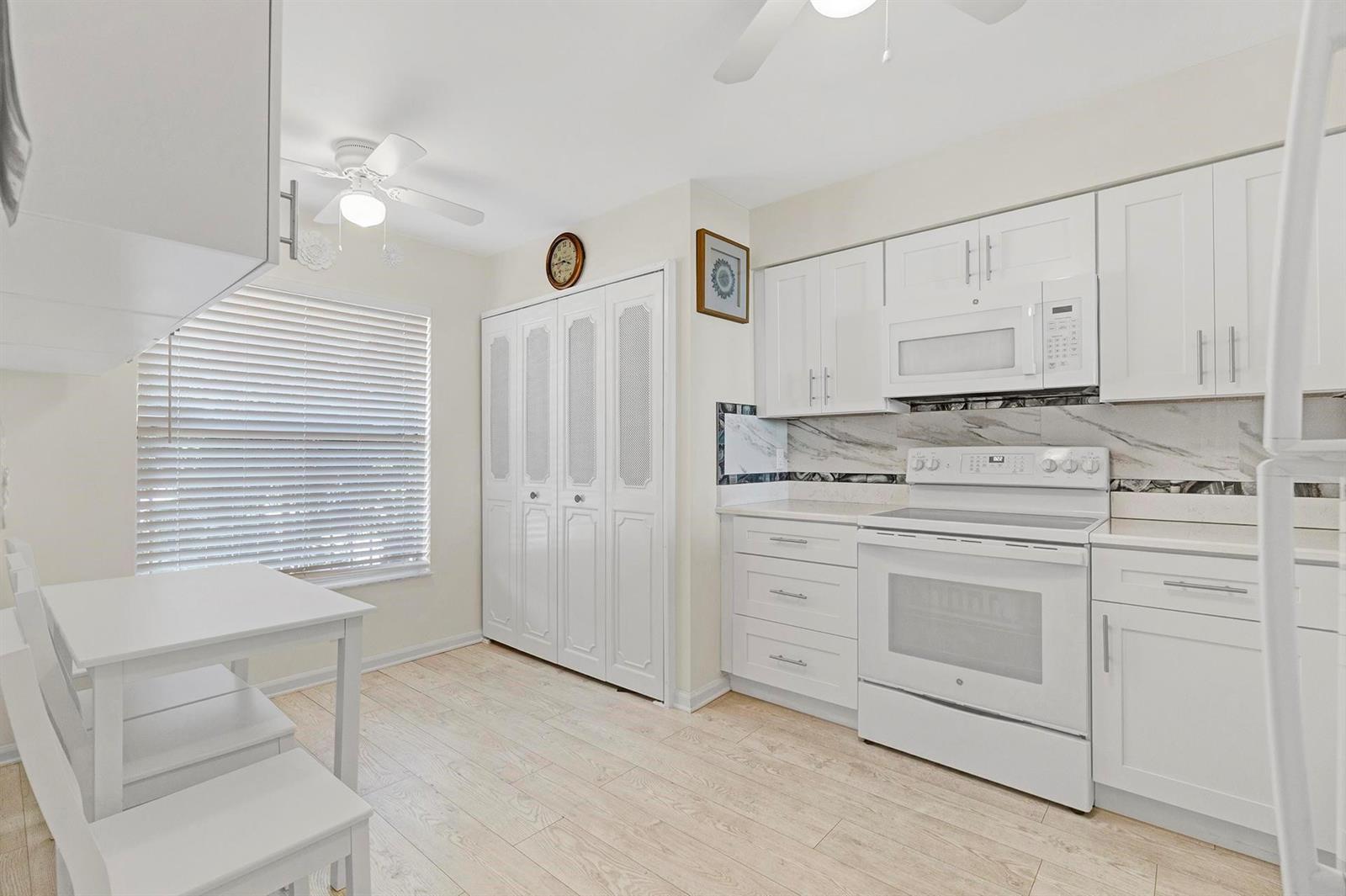 A bright kitchen features white cabinetry, a white stove, and a small dining area — 14575 Bonaire Boulevard # 202, Delray Beach FL 33446, DELRAY BEACH, FL