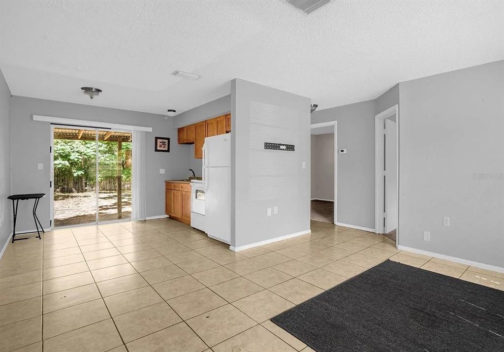 An open-concept living and kitchen area features tile flooring, light gray walls, and sliding doors — 15115 OMAHA STREET, HUDSON, FL