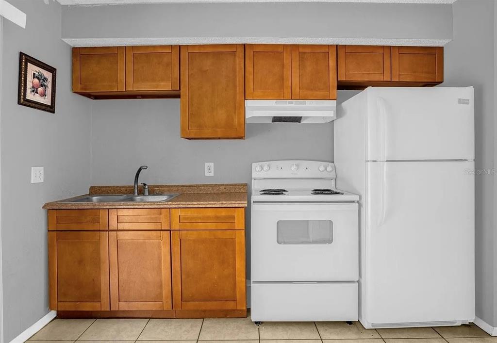 A kitchen features wooden cabinets, a white stove, a white refrigerator, and a sink — 15115 OMAHA STREET, HUDSON, FL