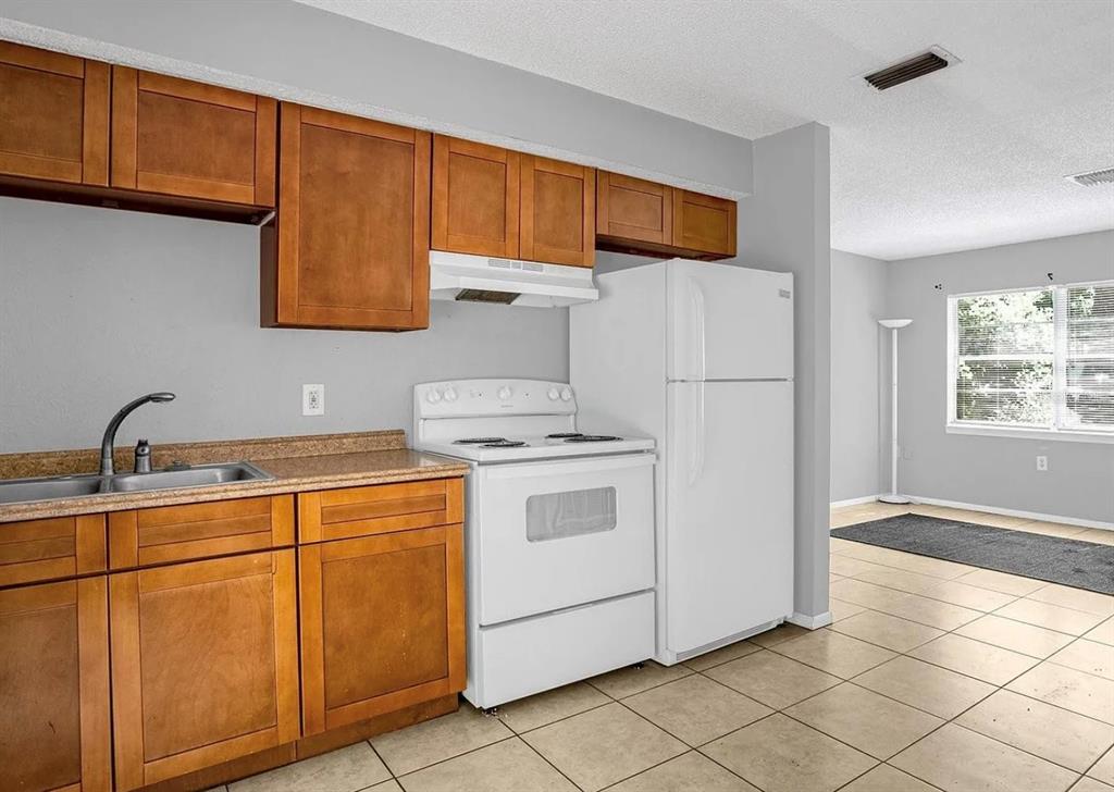A kitchen with wooden cabinets, white appliances, and tile flooring opens into a living area — 15115 OMAHA STREET, HUDSON, FL