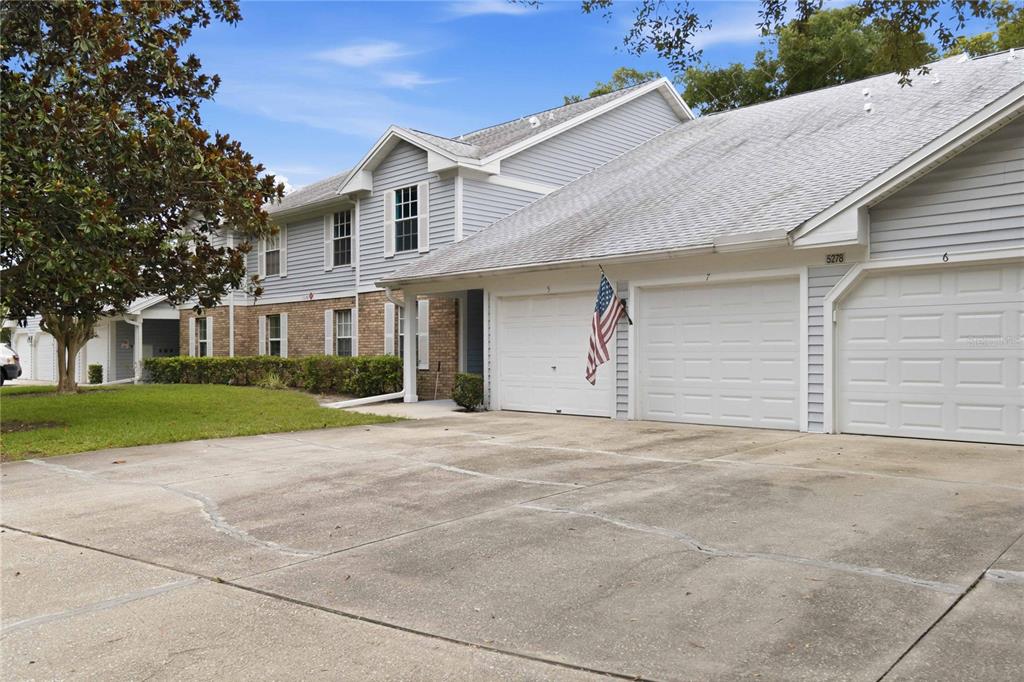 A two-story residential building with light gray siding, brick accents, and multiple garage doors — 5278 WHITSTABLE WAY UNIT 5, ORLANDO, FL