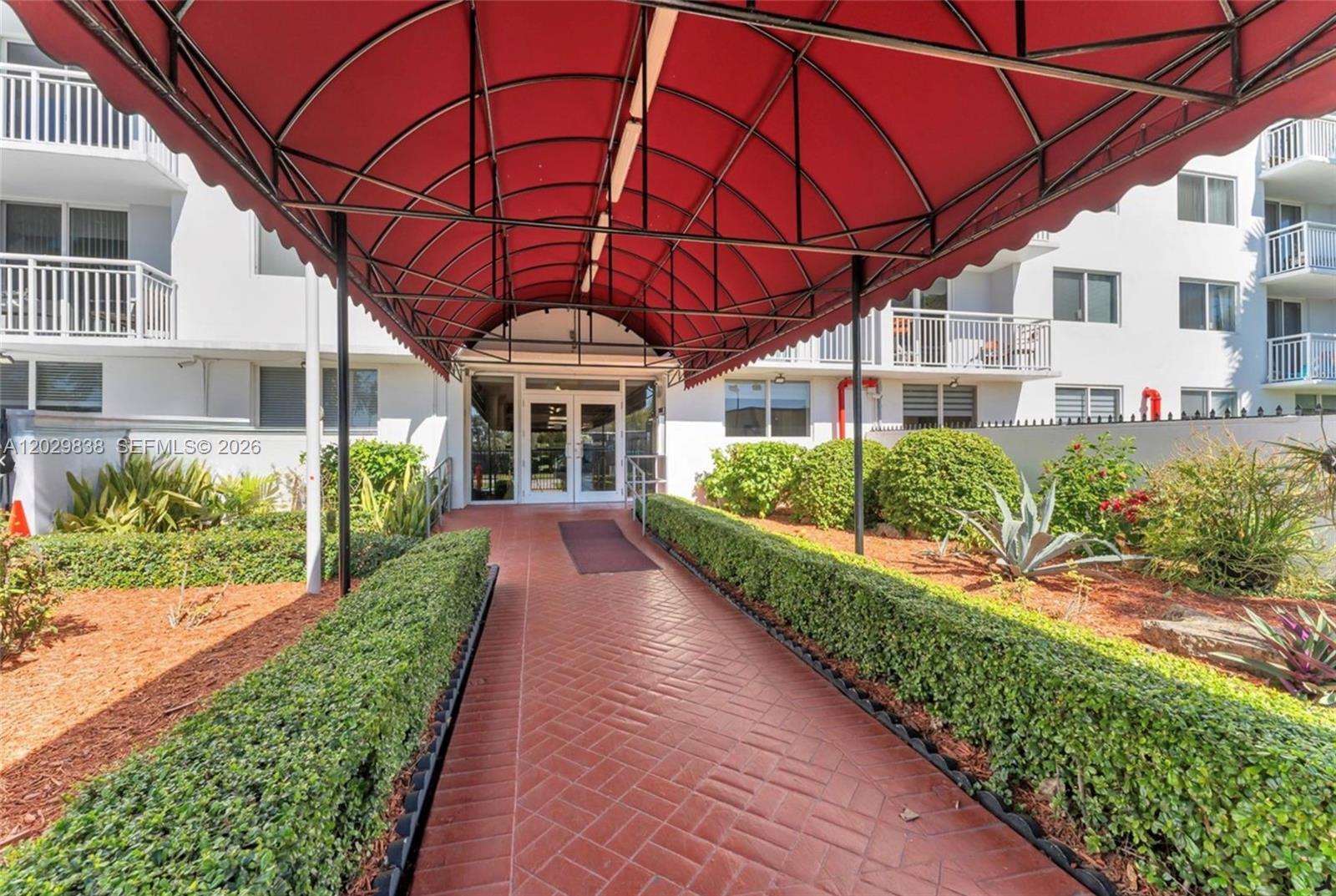 A red awning covers a brick walkway leading to the entrance of a white building — 1251 NE 108th St # 617, Miami FL 33161, MIAMI, FL
