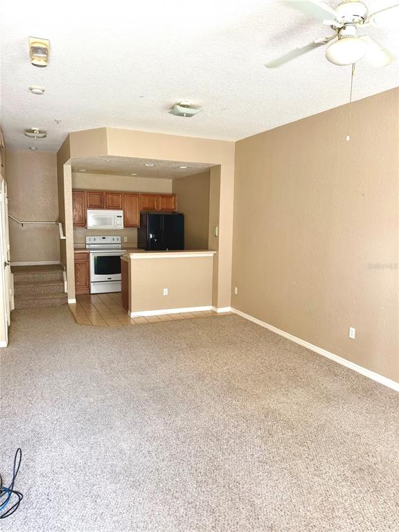 A living room with carpeted floors leads to a kitchen featuring wood cabinets and appliances — 2606 LODI CIRCLE UNIT 105, KISSIMMEE, FL