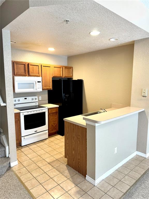 A kitchen features wood cabinets, white appliances, a black refrigerator, and a breakfast bar — 2606 LODI CIRCLE UNIT 105, KISSIMMEE, FL