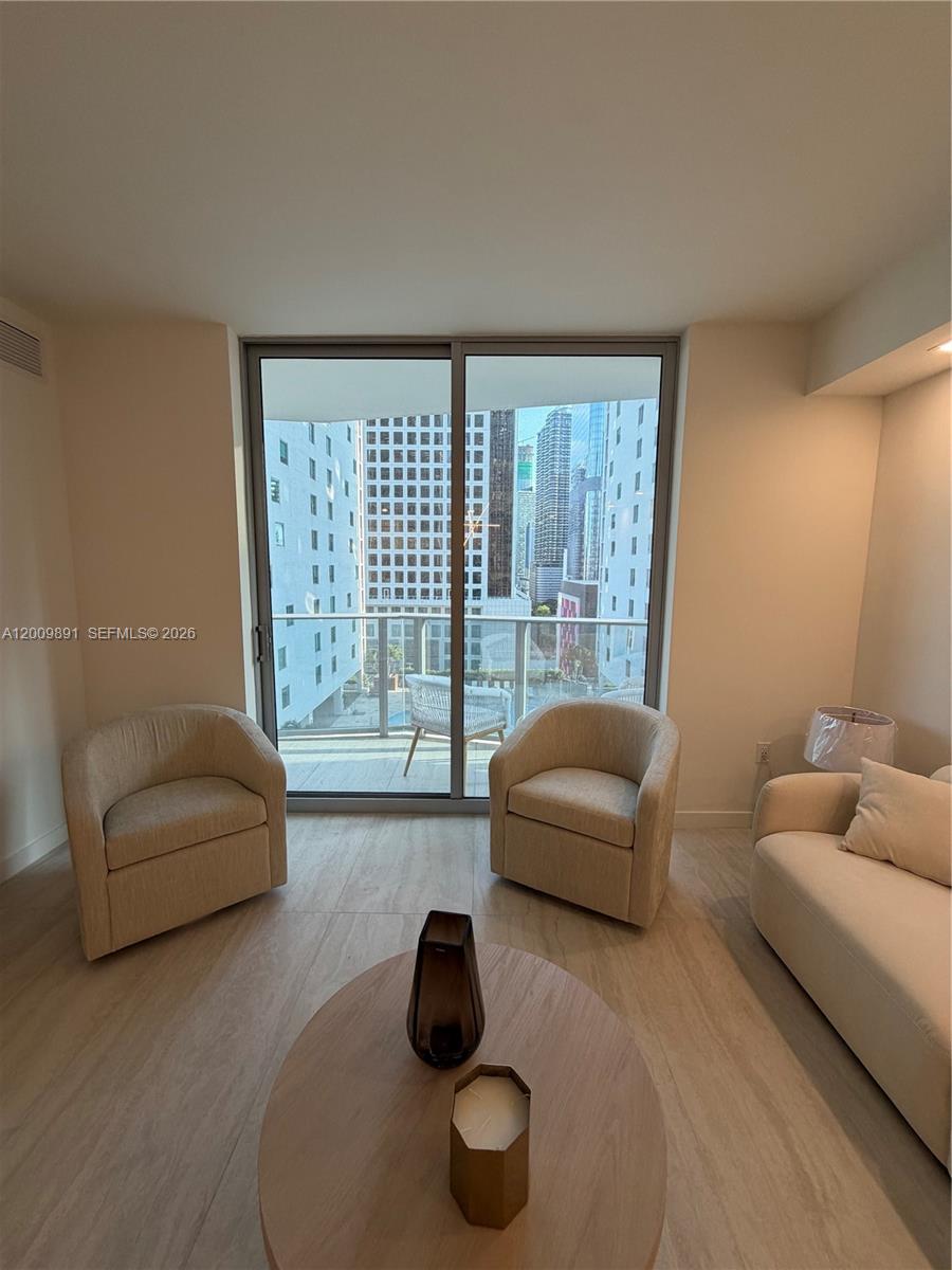 A living room features two beige armchairs, a coffee table, and a balcony with city views — 77 SE 5th street # 1614, Miami FL 33131, MIAMI, FL