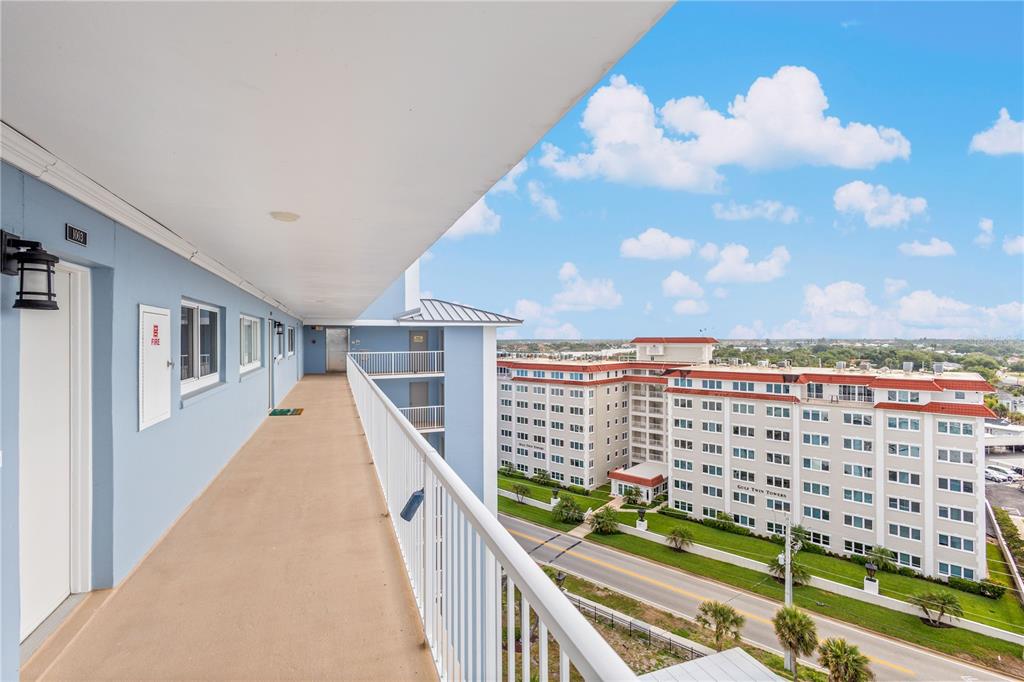 An exterior walkway overlooks a multi-story apartment building and a road under a blue sky — 555 THE ESPLANADE N UNIT 1003, VENICE, FL