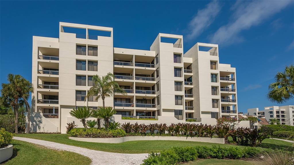 A multi-story white apartment building stands behind a landscaped lawn with palm trees — 1932 HARBOURSIDE DRIVE UNIT 244, LONGBOAT KEY, FL