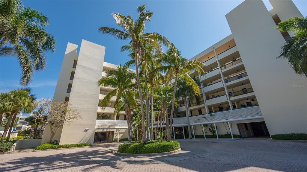 A multi-story beige apartment building features a circular driveway with palm trees in the center — 1932 HARBOURSIDE DRIVE UNIT 244, LONGBOAT KEY, FL