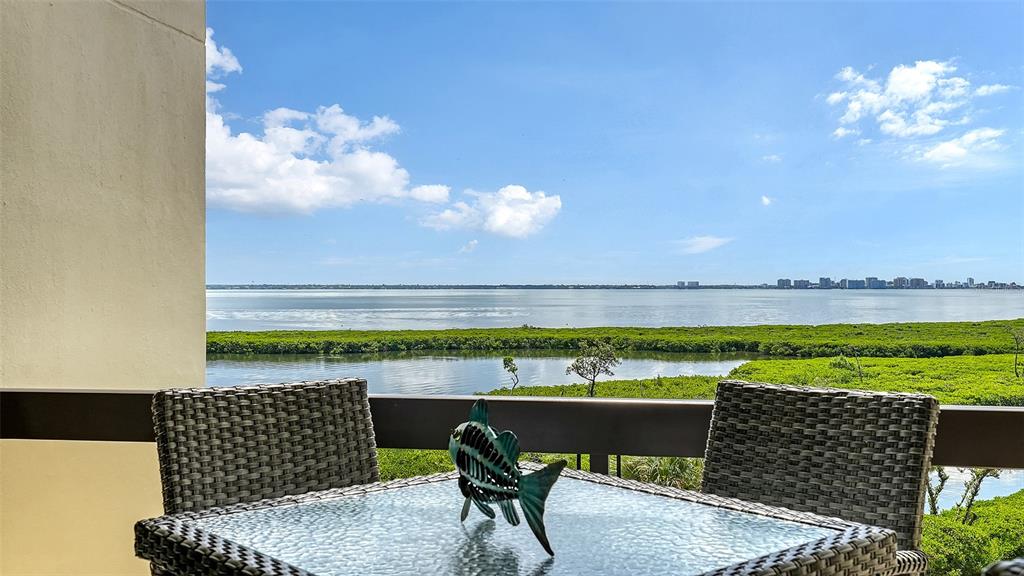 A balcony with a glass-topped table and wicker chairs overlooks a bay and mangroves — 1932 HARBOURSIDE DRIVE UNIT 244, LONGBOAT KEY, FL