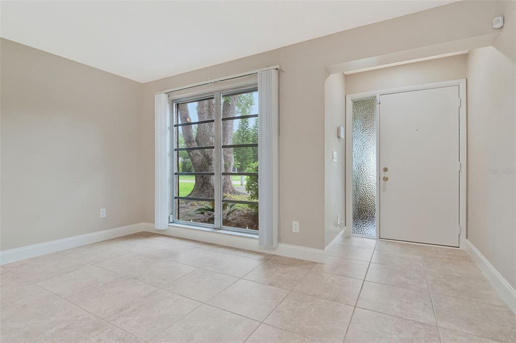 An empty room with beige tile floors, a large window, and a white front door — 2958 DUNDEE DRIVE, PALM HARBOR, FL