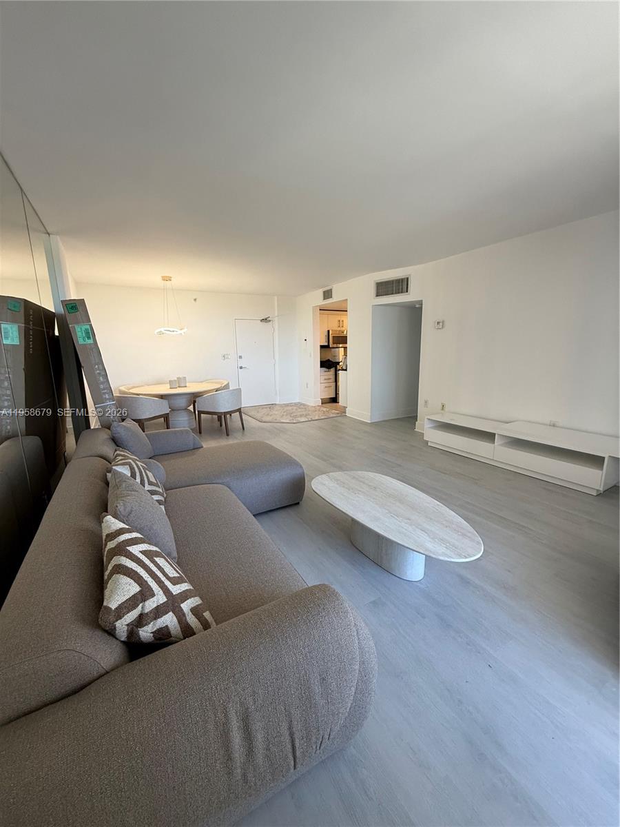 A living room features light wood flooring, a grey sectional sofa, and a white media console — 10275 Collins Ave # 420, Bal Harbour FL 33154, BAL HARBOUR, FL