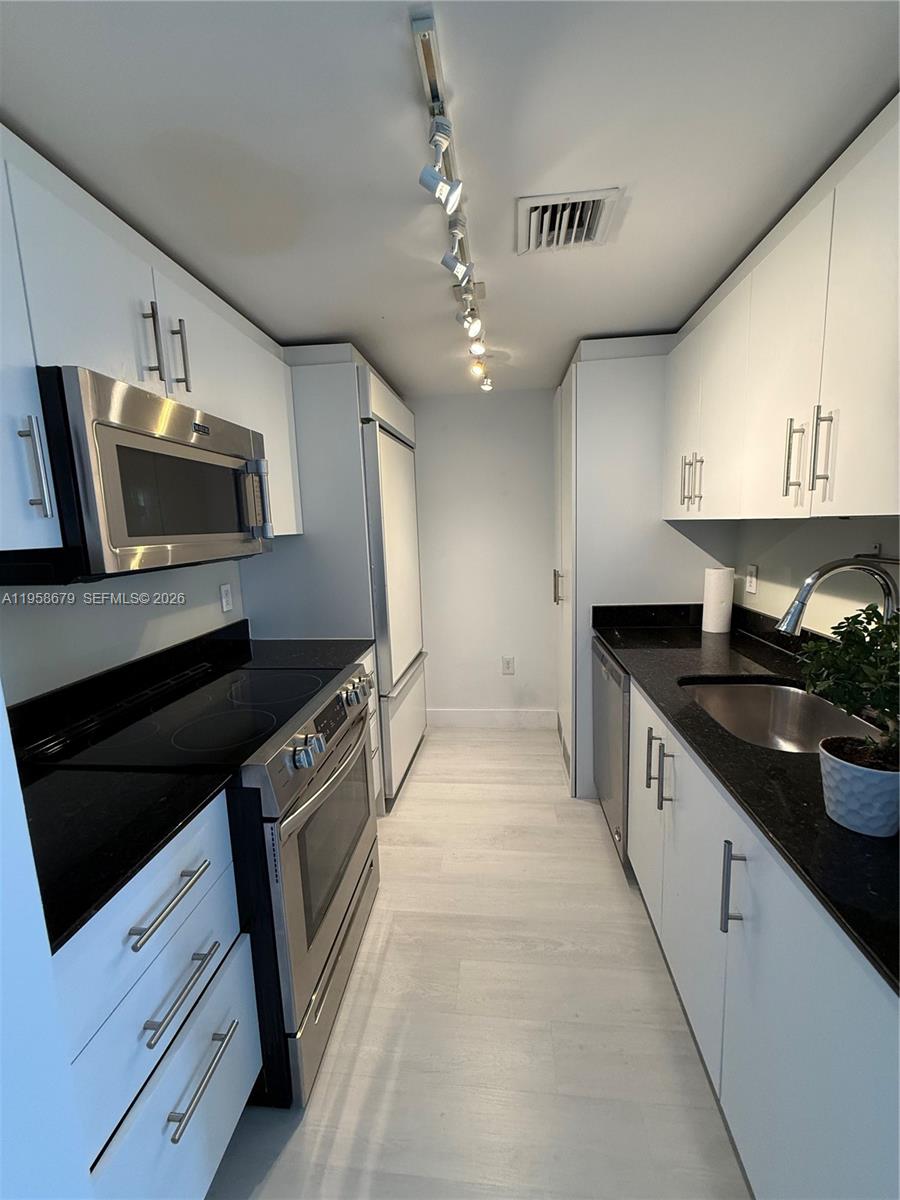A galley kitchen features white cabinets, black countertops, stainless steel appliances, and track lighting — 10275 Collins Ave # 420, Bal Harbour FL 33154, BAL HARBOUR, FL