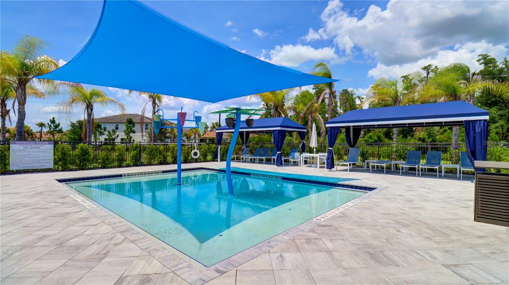 A swimming pool with a blue shade canopy and water features sits on a patio — 3338 GREAT BANYAN WAY, WESLEY CHAPEL, FL