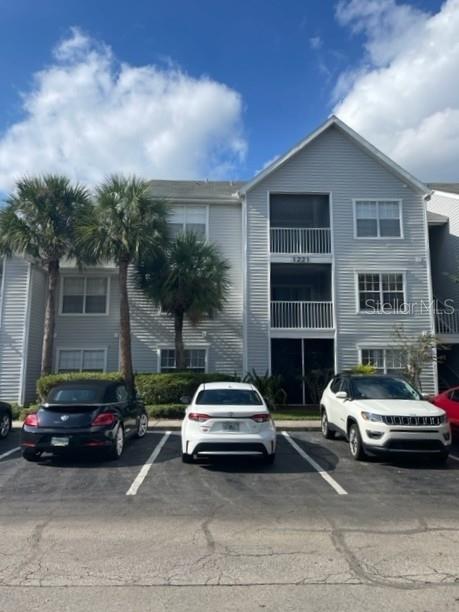 A three-story apartment building exterior with three parked cars in the foreground — 1221 BERMUDA LAKES LANE UNIT 202, KISSIMMEE, FL