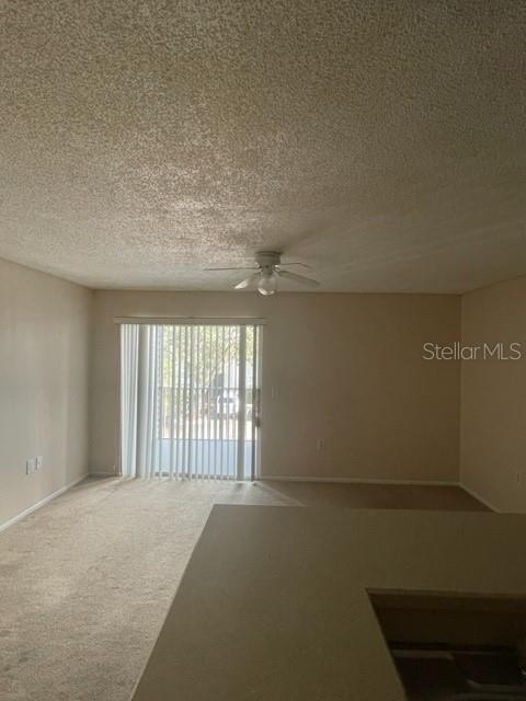 A carpeted living room features a ceiling fan and a sliding glass door with blinds — 1221 BERMUDA LAKES LANE UNIT 202, KISSIMMEE, FL