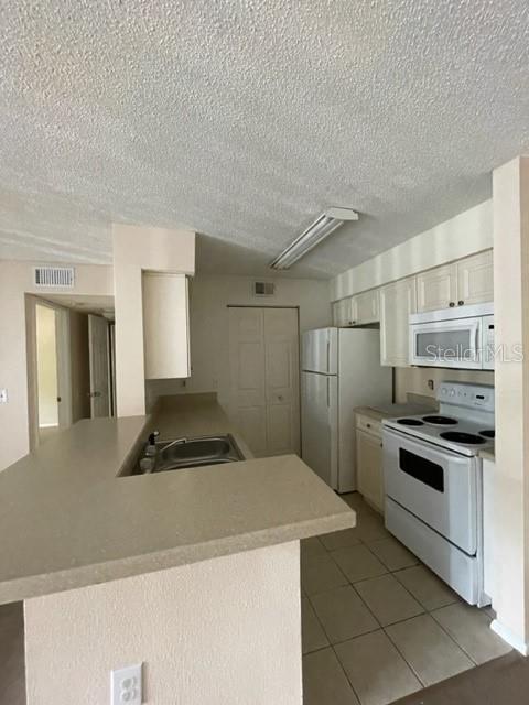 A kitchen features a breakfast bar, white appliances, and light-colored cabinetry — 1221 BERMUDA LAKES LANE UNIT 202, KISSIMMEE, FL