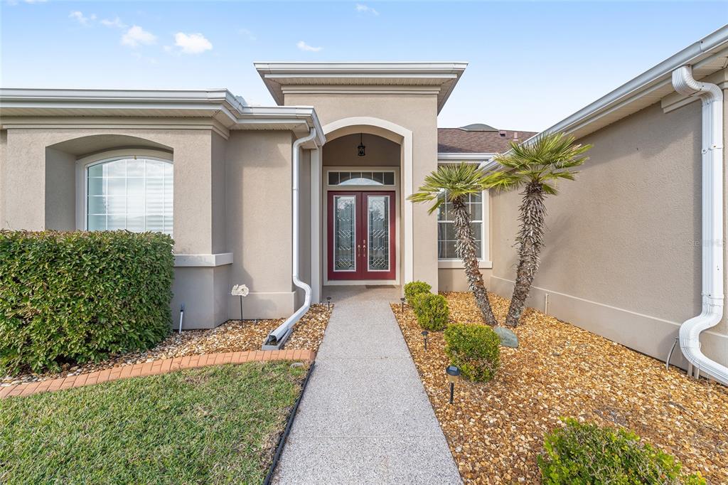 A concrete walkway leads to the double front doors of a tan stucco house — 9479 SE 130TH STREET ROAD, SUMMERFIELD, FL