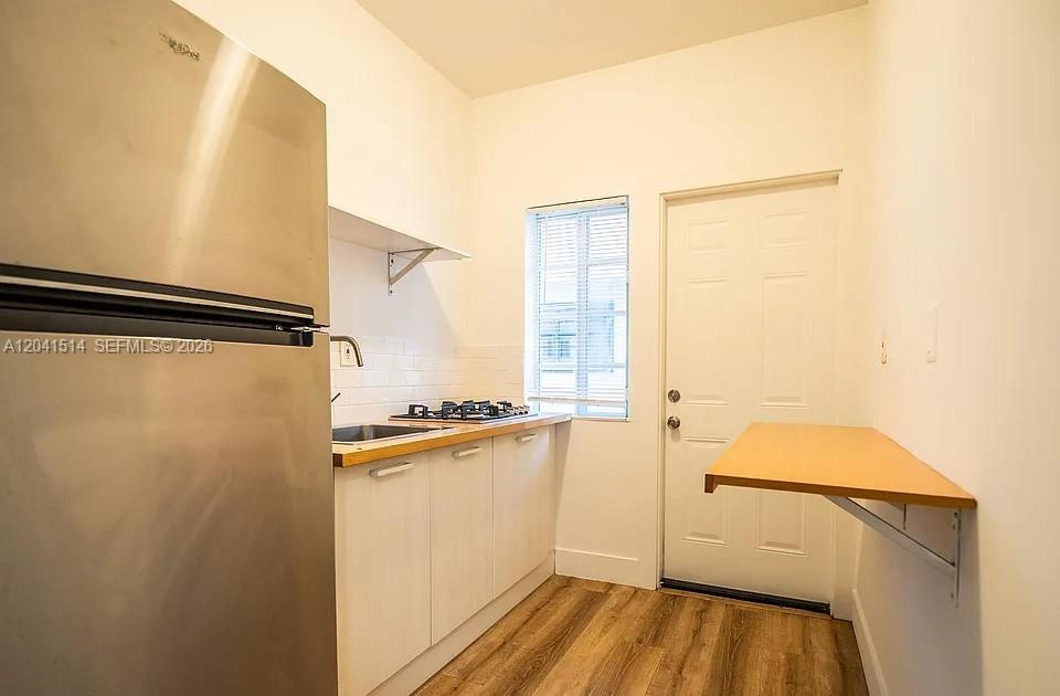 A small kitchen features white cabinets, a stainless steel refrigerator, and a wall-mounted breakfast bar — 245 79th Street # 2, Miami Beach FL 33141, MIAMI BEACH, FL