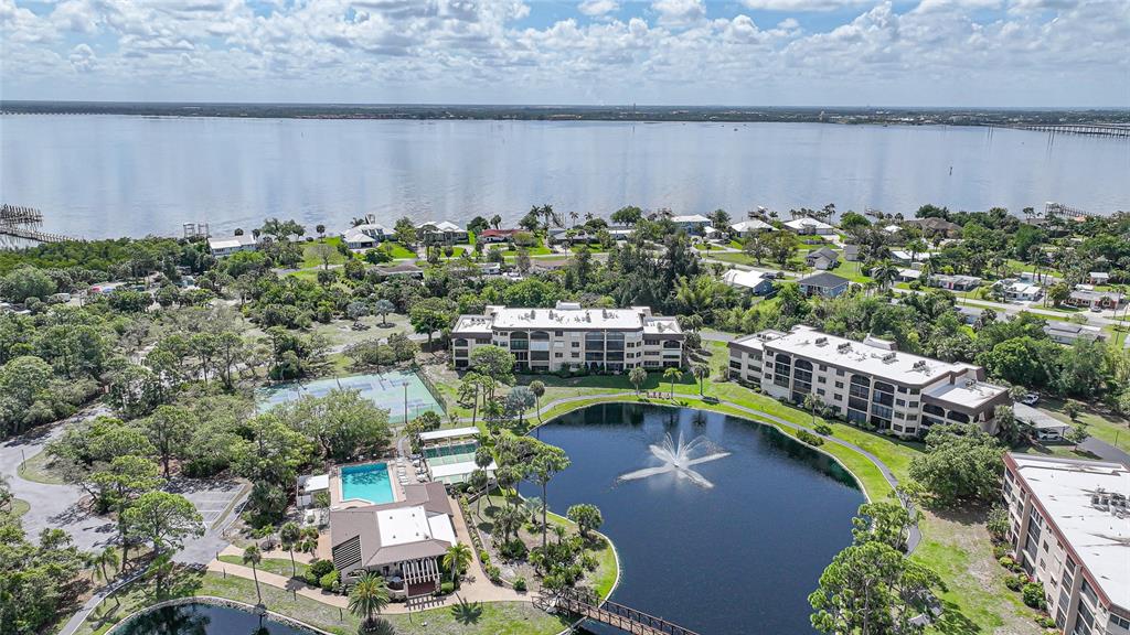 An aerial view shows apartment buildings, a swimming pool, tennis courts, and a fountain-filled pond — 23465 HARBORVIEW ROAD UNIT 616, PUNTA GORDA, FL