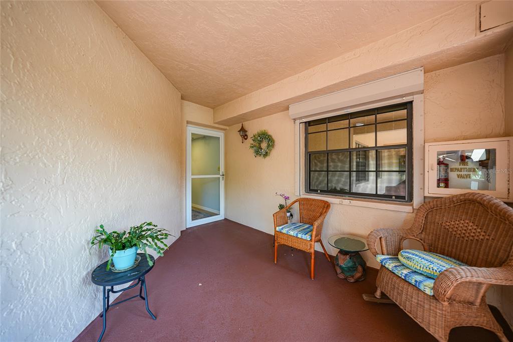 A covered patio features a red floor, two wicker chairs, a small table, and a window — 23465 HARBORVIEW ROAD UNIT 616, PUNTA GORDA, FL