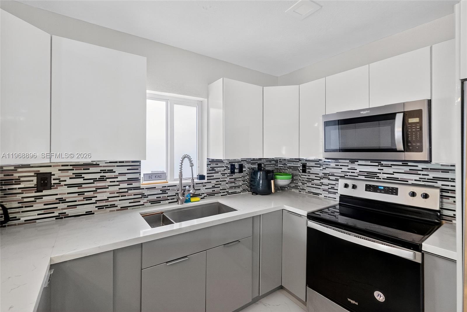 A modern kitchen with gray cabinets and a white countertop overlooks a dining area — 231 NW 44th St, Miami FL 33127, MIAMI, FL