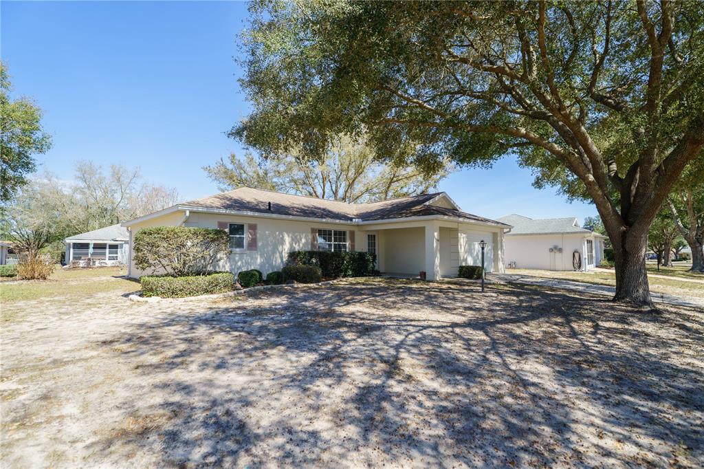 A single-story house with a beige exterior, a covered entryway, and a large oak tree — 9859 SW 97TH LANE, OCALA, FL
