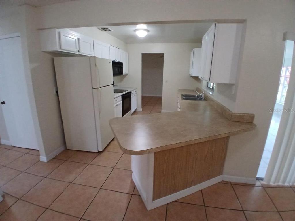 A kitchen features white cabinets, a white refrigerator, and a tan countertop peninsula — 632 MIDIRON DRIVE, POINCIANA, FL