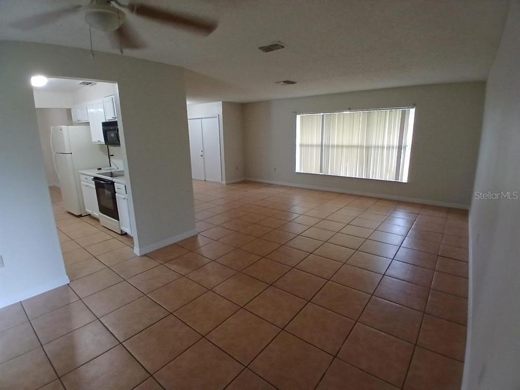 An open-concept living area with tile flooring leads into a kitchen with white appliances — 632 MIDIRON DRIVE, POINCIANA, FL