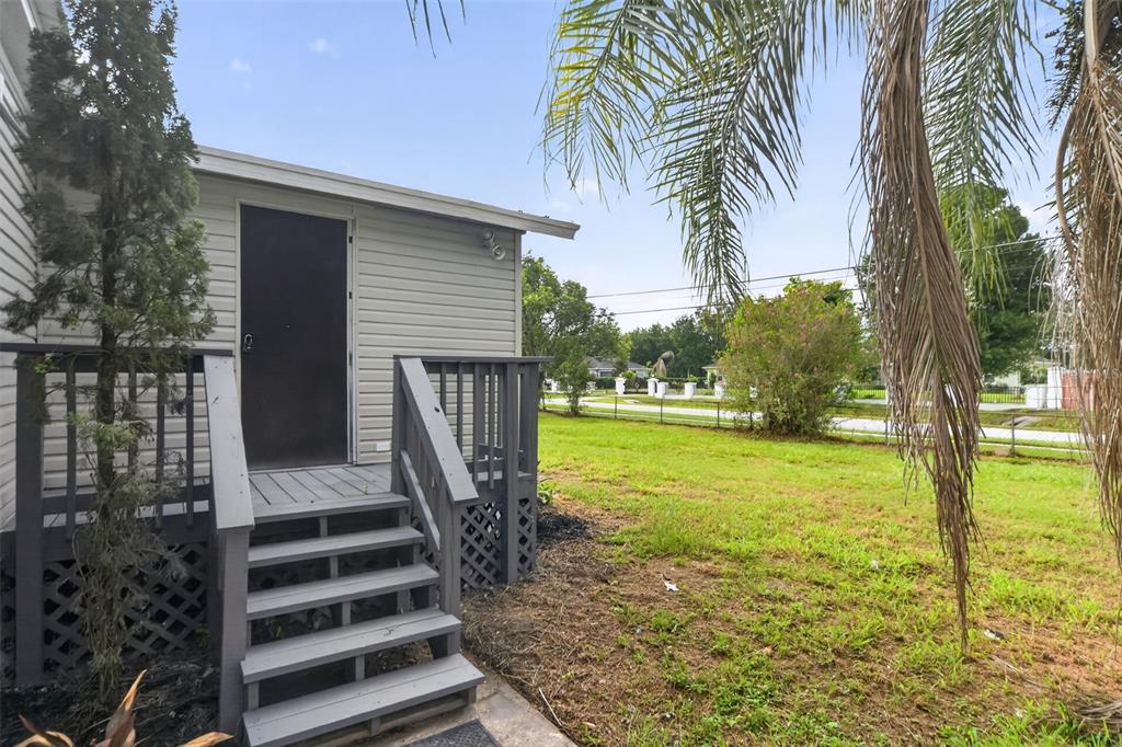 A gray wooden deck with stairs leads to a side door of a light-colored house — 10213 UNION PARK DRIVE, ORLANDO, FL